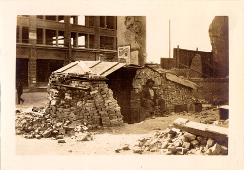 [Man sitting at a makeshift street kitchen on an unidentified street]