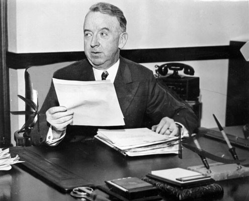 [Thomas Brooks at his desk with papers]