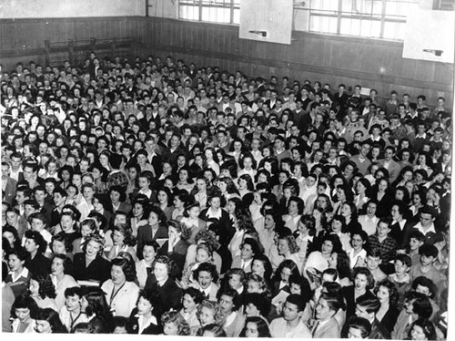 [Large group of students standing in Lowell High School's gym for the Woruth War Loan rally]