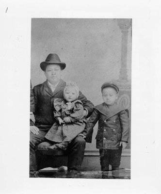 [Lew Hing, with his daughter Rose Lew Moon on his knee, and one of his son's standing at his side]