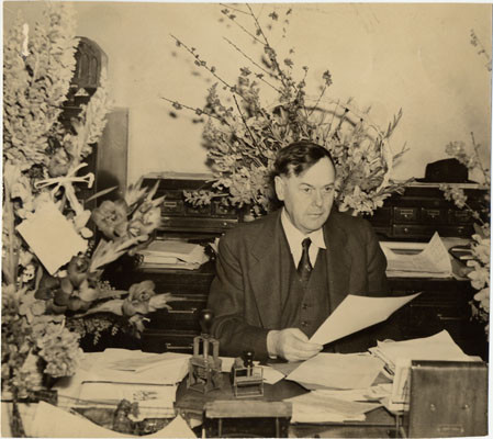 [Capt. Bernard J. McDonald at his desk surrounded by bouquets of flowers]