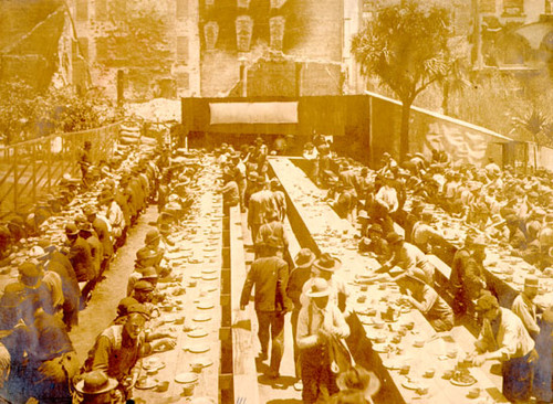 [workers sitting down for a meal in Union Square, St. Francis Hotel in background]