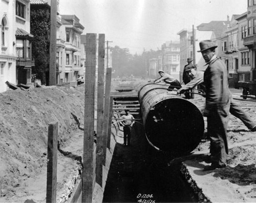 [Construction workers lowering pipe into trench along Sixth Avenue and Irving Street]