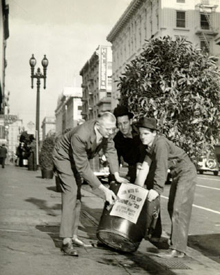 [Three men carrying a tree with planter with a sign attached to planter that reads 'Join With Us Fix Up Shine For '39']