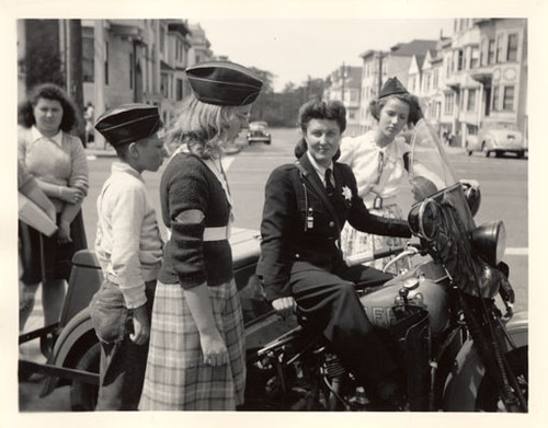 [Patrolwoman sits on her three wheeled motorcycle while talking with young people]