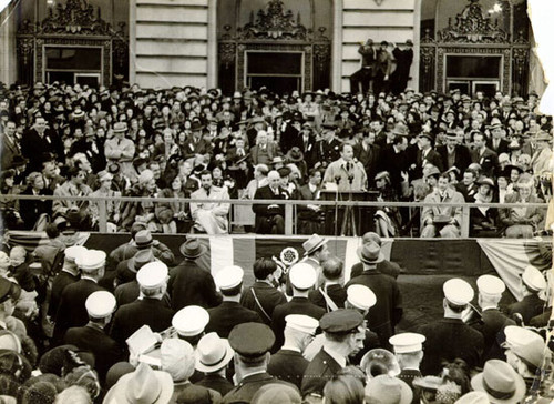 [Darryl Zanuck standing in front of City Hall speaking to a crowd of people flanked by Mayor Rossi and some actors from the Hollywood community]