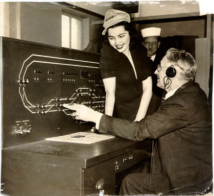 [Three unidentified people in a control room for the San Francisco-Oakland Bay Bridge electric railway system]