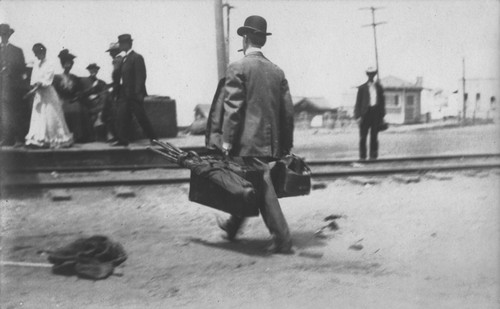 Unidentified man showed here carrying suitcases and golf clubs after arriving on the train at the La Jolla Railway Station. Circa 1905