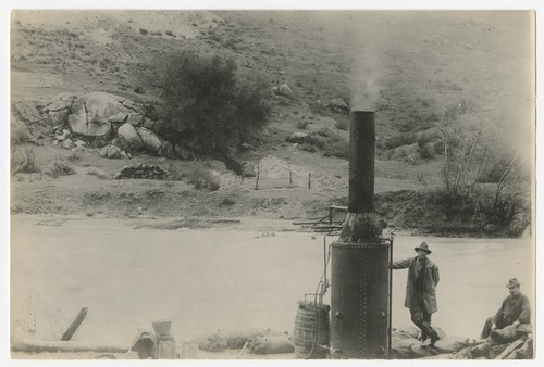 Two men with machinery by river