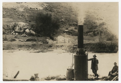 Two men with machinery by river