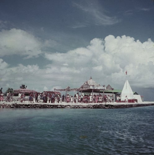 People at a French Polynesian pier with a sign reading "Bienvenue M. et Mme. Le Goveneur"