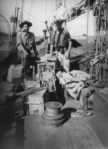 [Two men standing surrounded by supplies on deck of R/V E.W. Scripps]