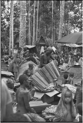 Mortuary ceremony, Omarakana: women unfold mats, covering banana leaf bundles from rain