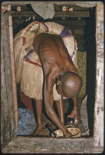Woman in long fiber skirt, her head shaved as sign of mourning, with mortar and pestle for betel nut