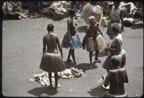 Mortuary ceremony: women exchange banana leaf bundles and long fiber skirts, one woman wears shell necklace with white cowries, talcum powder on shoulders