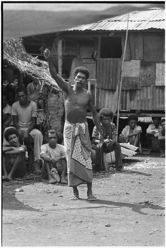 Meeting: man speaks in front of gathered crowd, his arm raised