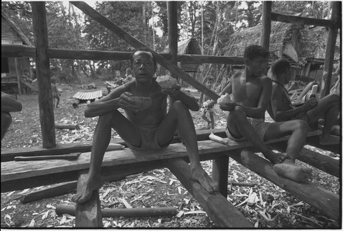 House-building: men share meal of yams, in building under construction