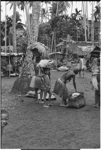 Mortuary ceremony, Omarakana: mourning women and children carry fiber skirts and baskets of banana leaf bundles for ritual exchange