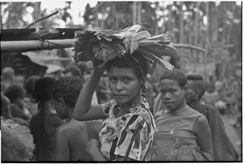 Mortuary ceremony, Omarakana: woman in Western-style blouse, carries banana leaf bundles on her head at ritual exchange