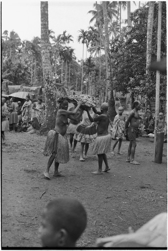 Mortuary ceremony, Omarakana: women, faces and bodies blackened with ash, heads shaved, carry large basket of yams