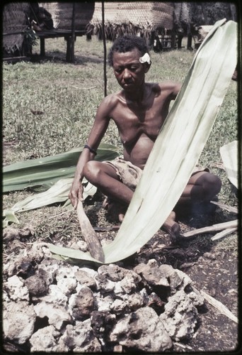 Woman heats and flattens pandanus leaf over a fire, softening it for use in weaving