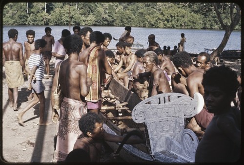 Canoe-building: people gathered for dedication of new canoe, Mogiovyeka (foreground) working with an adze behind a whitewashed prowboard