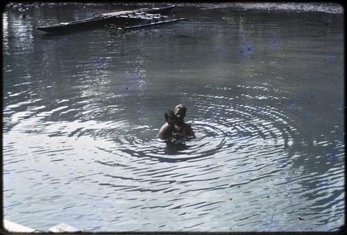 Manus: child and adult bathe in lagoon, canoe in background