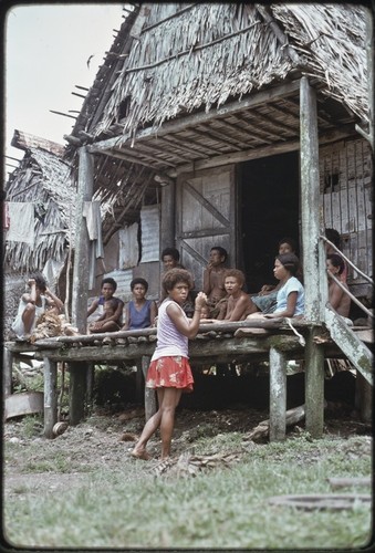 Mortuary ceremony: woman (l) has brought banana leaf bundles for exchange ritual, group of women on house veranda