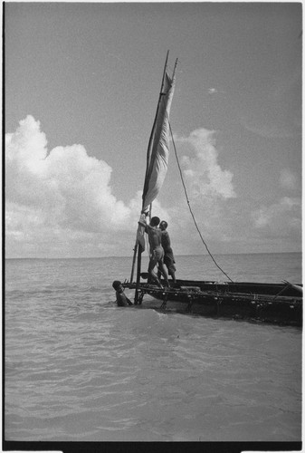 Canoes: men raise sail on an outrigger canoe