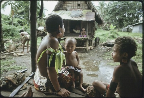 Adolescent girl wears decorative skirt, fragrant leaves, turtle shell earrings, younger girl (right) is similarly attired