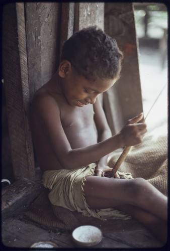 Child grinding betel nut with mortar and pestle