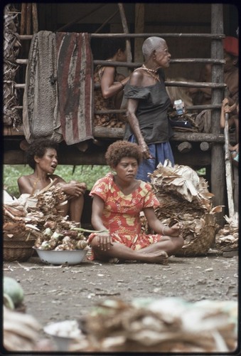 Mortuary ceremony: woman with baskets heaped with banana leaf bundles, bowl of uncooked taro