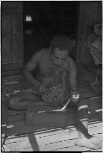 Canoe-building: man uses an adze to smooth small piece of wood for canoe part