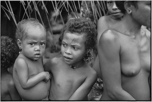 Mortuary ceremony, Omarakana: girl (r) has mourning ash on face and wears turtle shell earrings, baby looks at camera with concern