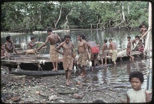 Fishing: men carry strings of fish that they have obtained via exchange or barter from returned fishermen