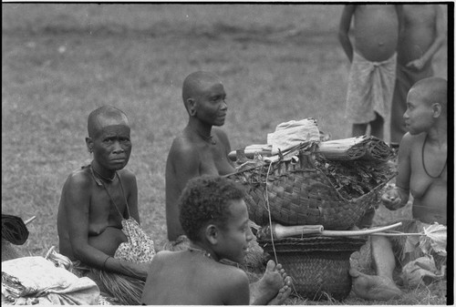 Mortuary ceremony: mourning women, faces and bodies painted black, beside a basket filed with banana leaf bundles