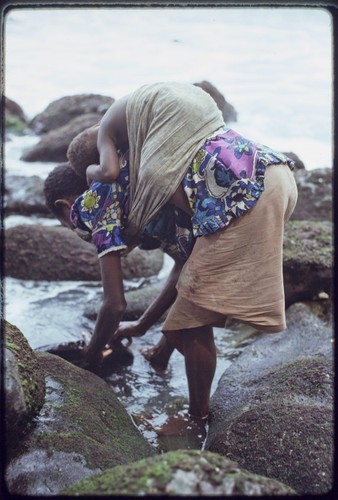 Kairiru: woman rinses a pan, small child in a sling on her back