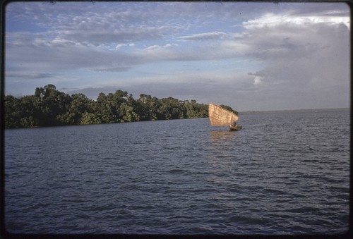 Canoe with sail up, near a small island