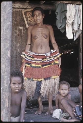 Woman wearing decorated banana fiber skirt valuable over a longer skirt, picture of Jesus (background)