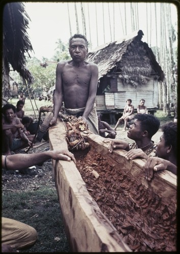 Canoe-building: man (center) says a spell while cutting vine rope from the hollowed out log