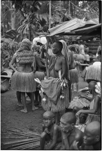 Mortuary ceremony, Omarakana: woman with crossed necklace and shaved head, carries basket that belonged to deceased man, adorned with cowry shells and other valuables