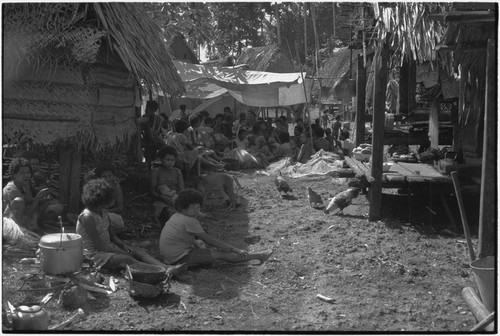 Mortuary ceremony: women weave long fiber skirts for ritual exchange, women in foreground tend cooking pots over fire