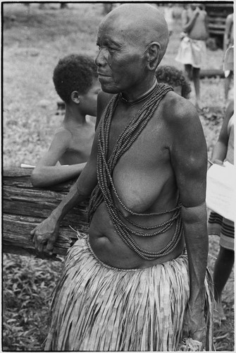 Mortuary ceremony: mourning woman with shaved head wearing long fiber skirt and beaded necklaces