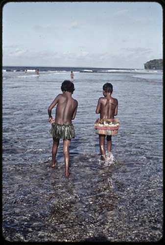 Girls walk in shallow water near coral reef edge near Wawela village