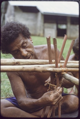 Canoe-building: man attaches outrigger float to a canoe, lashing with lengths of vine