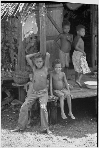 Children on veranda, taro plants and basket in background