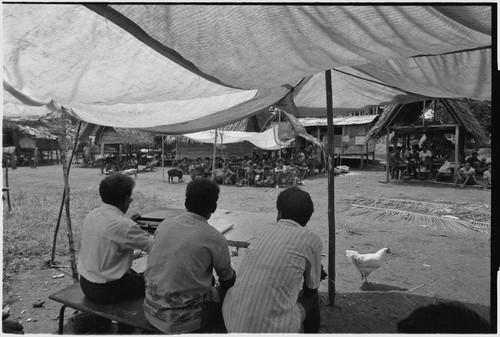 Meeting: men at a table, people gathered facing them