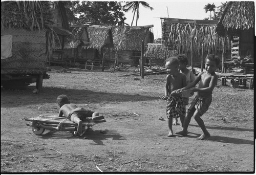 Children playing, pulling boy on a makeshift cart in Tukwaukwa village, Kiriwina