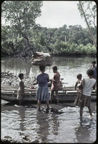 Canoes: women load items onto canoe used for coastal transport, woman (center) holds basket of banana leaf bundles on head