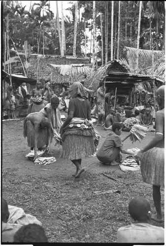 Mortuary ceremony, Omarakana: mourning women count banana leaf bundles for ritual exchange, woman in center wears decorated fiber skirt